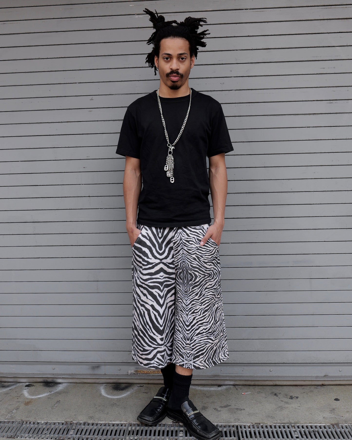 Person wearing a black t-shirt and zebra print pants standing in front of a closed shutter.