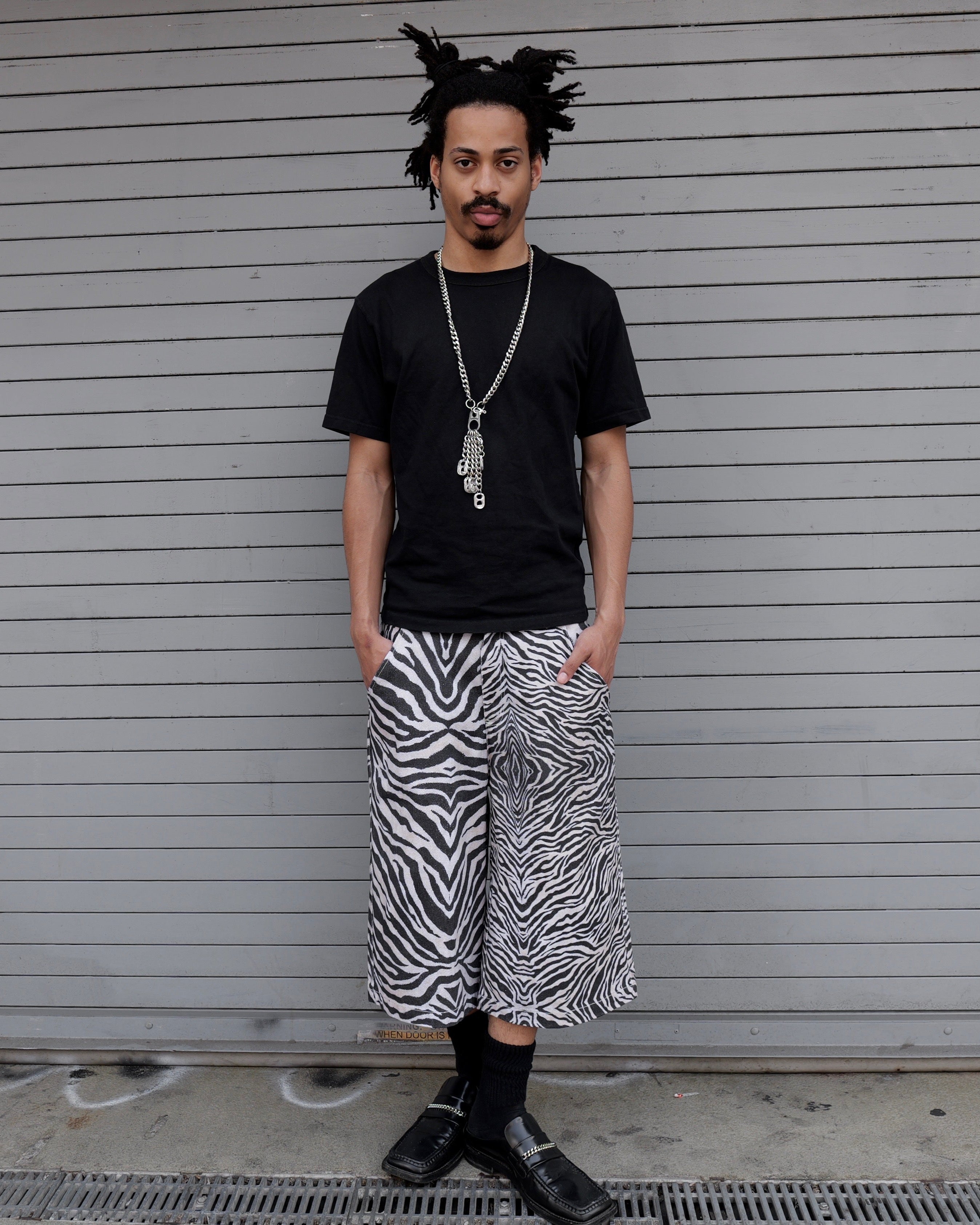 Person wearing a black t-shirt and zebra print pants standing in front of a closed shutter.