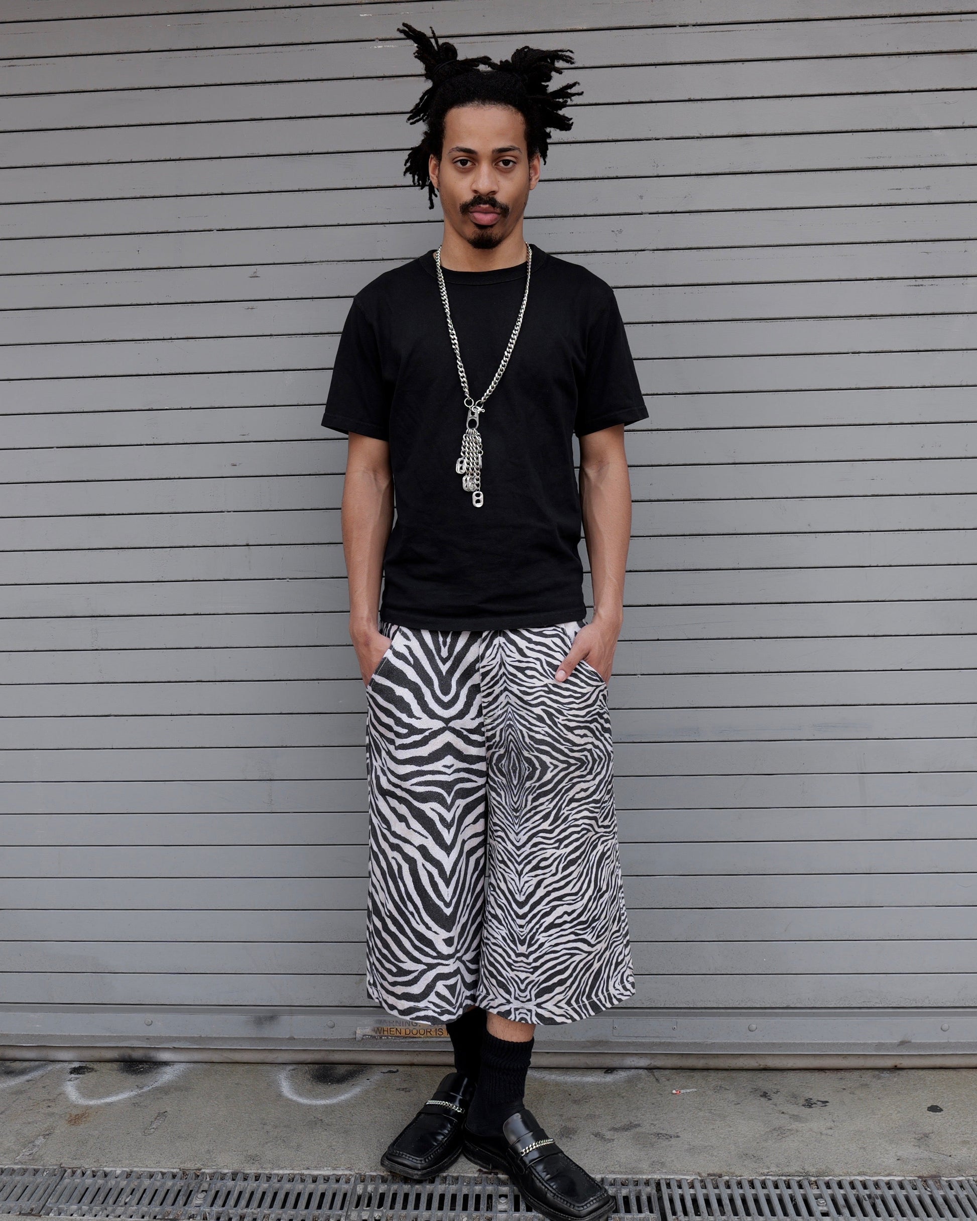 Person wearing a black t-shirt and zebra print pants standing in front of a closed shutter.